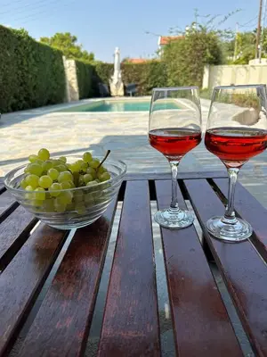 two glasses of wine and a bowl of grapes on a wooden table at Villa Agia Marina 5m walk to the beach with private pool in Aghia Marina
