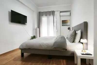 a white bedroom with a bed and a window at Velora Apartments in Athens