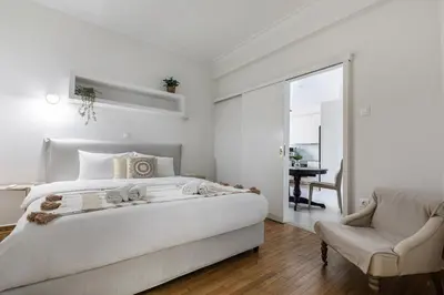 a white bedroom with a large bed and a chair at Attica - Captivating 2-Bedroom Apt & Balcony in Athens in Athens