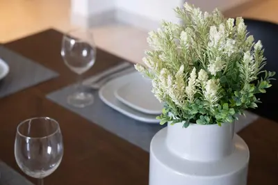 a white vase with white flowers on a table with glasses at Modern Apartment in Piraeus Port D2 in Piraeus