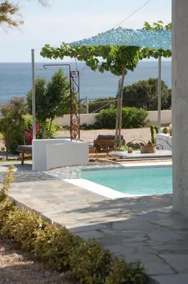 a swimming pool with an umbrella next to the ocean at Aegean Grace in Áyios Dhimítrios
