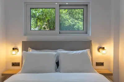 two windows above a bed with two white pillows at The Secret Garden Stay in Athens