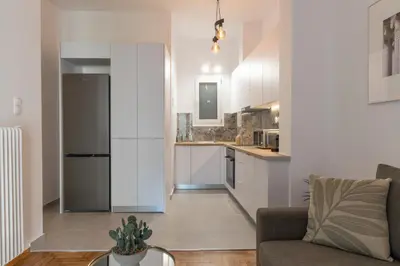 a kitchen with white cabinets and a living room at Fresh 2 bdrm Apt in Koukaki in Athens