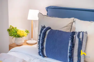 a bed with a blue headboard and a lamp on a table at Bright, Central Hideaway Near Acropolis & Metro! in Athens