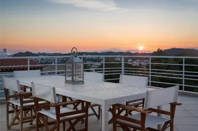 a white table and chairs on a balcony with the sunset at Vouliagmeni Exclusive Residence in Athens