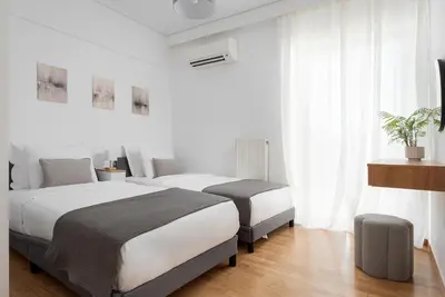two beds in a bedroom with white walls and wood floors at Majestique South Riviera Residence in Athens