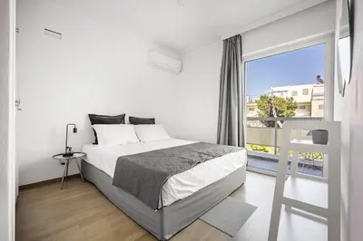 a white bedroom with a bed and a large window at Varkizaki by the sea in Varkiza