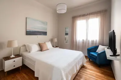 a white bedroom with a bed and a blue chair at Relax & Comfy 2BR Apt Close To Athens Center in Athens