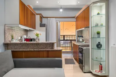 a kitchen with wooden cabinets and a gray couch at Adigonis Apartment next to the metro station in Athens