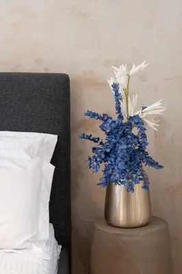 a vase with blue and white flowers on a table next to a bed at Piraeus Home in Piraeus
