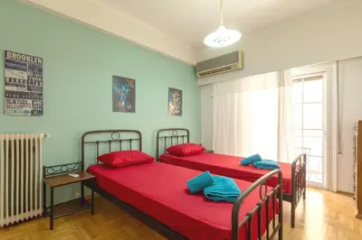 two beds in a room with red sheets and blue pillows at Athens center traditional & classic 2BR apartment in Mesochórion