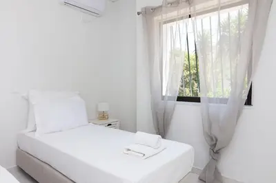 a white bedroom with a white bed and a window at Villa Svoronou Athens Riviera in Áyios Nikólaos