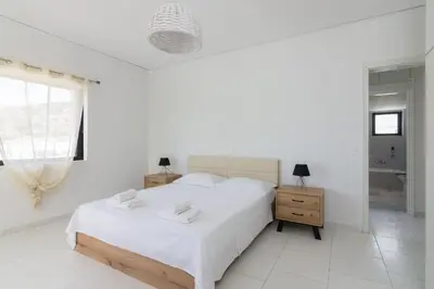 a white bedroom with a large bed and a window at Villa Svoronou Athens Riviera in Áyios Nikólaos