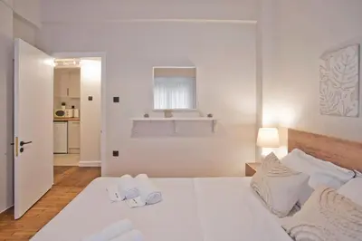 a white bedroom with a white bed and a kitchen at Historic Boutique Apartment in Artists' Kipseli in Athens