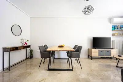 a dining room with a table and chairs and a tv at Glyfada Muse - Sea and City Apartment in Athens