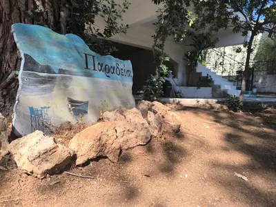 a bench sitting in front of a tree with rocks at Silver Paradeisi Apartment in Palaiá Fókaia