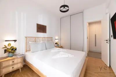 a bedroom with a large white bed and a wooden nightstand at Coastal Charm at Pasalimani - Steps from Port&Beach in Piraeus