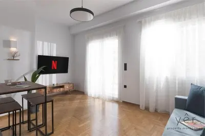 a white living room with a table and a tv at Coastal Charm at Pasalimani - Steps from Port&Beach in Piraeus