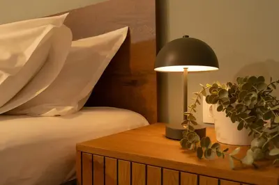 a lamp on a wooden table next to a bed at Joo Nest - Your home near Piraeus Port in Piraeus