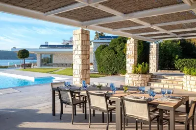 a table and chairs on a patio with a pool at Paradise Beachfront Villa Athenian Riviera in Aghia Marina