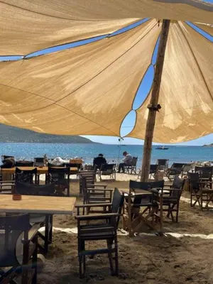 a group of tables and chairs under an umbrella on the beach at Christiana Luxury Apartments in Palaiá Fókaia