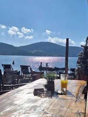a wooden table with a drink on it next to a lake at Christiana Luxury Apartments in Palaiá Fókaia