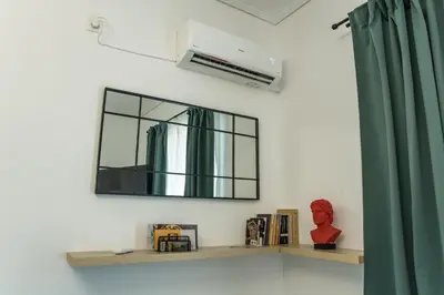 a mirror on a wall next to a shelf with books at Asclepius apartment Athens Airport in Spáta