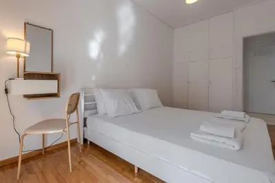 a white bedroom with a white bed and a chair at Bright 2BR Apt, Athens Base Near Sea & City in Athens