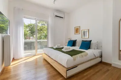 a white bedroom with a large bed with blue pillows at Artsi - Vibrant 3-BR Apartment & Balcony in Athens in Athens