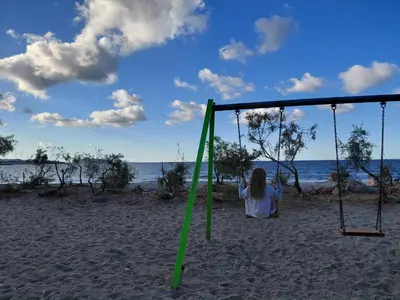 a woman sitting on a swing on the beach at S&M Cozy Garden Lagonissi in Lagonissi