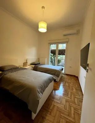 a bedroom with two beds and a tv and a window at Modern Glyfada Apartment Sleeps 6, 5min Walk to Beach in Athens