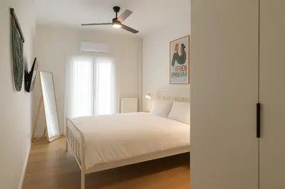 a white bedroom with a bed and a ceiling fan at 1BR Designer Apt Next To Metro & 15 minutes to Acropolis in Athens