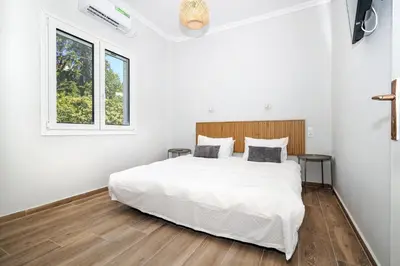 a white bedroom with a large white bed and a window at Muse Studios & Apartments Escape in Agia Marina Aegina