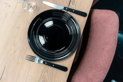 a black plate on a wooden table with a fork and knife at Lovely Goudi Apartment - Perfect Athens Getaway in Athens