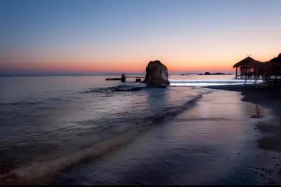 a beach with a rock in the water at sunset at Saroné Villa in Anavissos
