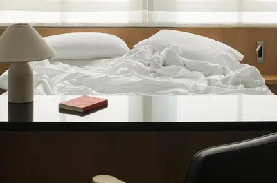 a bed with white sheets and a book on a table at P28 Suite 103 in Athens