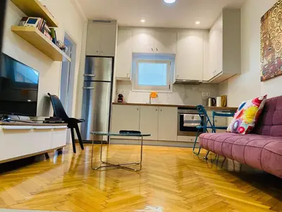 a living room with a purple couch and a kitchen at In the heart of Athens overlooking Kalligas Square! in Athens