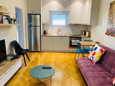 a living room with a purple couch and a kitchen at In the heart of Athens overlooking Kalligas Square! in Athens