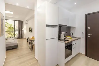 a kitchen with white cabinets and a living room at Athenian Nest Studio by WeHost Athens in Athens