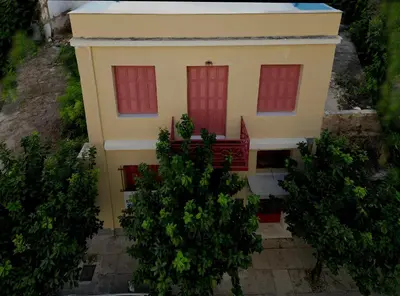 a small yellow house with red windows and trees at Back to the 50's near metro by Traser in Athens