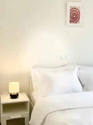a bed with white sheets and a lamp on a night stand at Glifada Luxury Two-Bedroom Suite in Athens