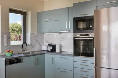 a kitchen with white cabinets and a stainless steel refrigerator at Deep Blue Luxury Escape Heated Pool & Sea View in Saronida