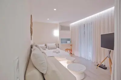 a white living room with a white couch and a tv at Radiant Voula Studio, a stone's throw from the Sea in Athens