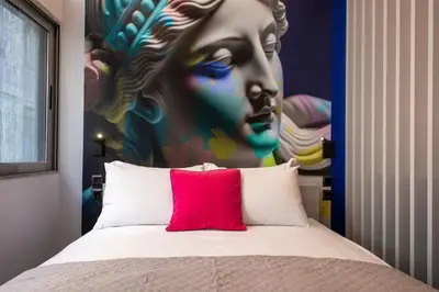 a bed with a red pillow in front of a painting at Morfes studio at historic center-near Acropolis in Athens