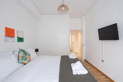a bedroom with a white bed and a flat screen tv at Cozy Apartment in Athens with Balcony, 5 min to Metro in Athens