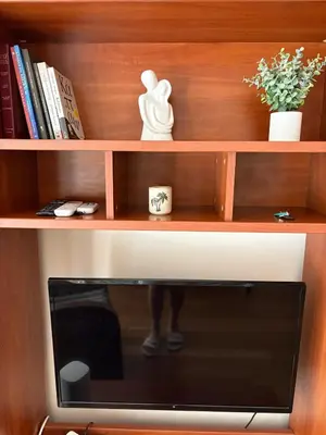 a television on a wooden shelf with a person standing behind it at Bright Koukaki Studio -10 min Walk to Acropolis in Athens