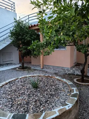 a garden with trees and rocks in front of a building at Daskalio Waves Appartment Filias in Dhaskalión