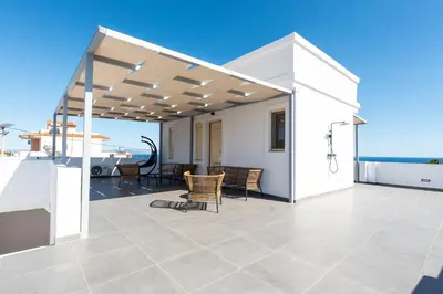 a white house with a patio with a view of the ocean at AeroHill Suites Near Athens Airport By SEM in Artemida