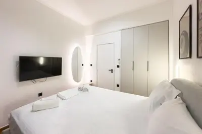 a white bedroom with a large white bed and a tv at Athenian Zen Suite in Athens