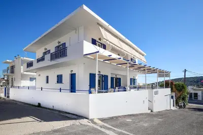 a white house with blue doors and a fence at Villa El Greco Apartments in Agia Marina Aegina